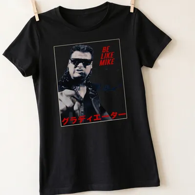 Bold graphic tee featuring wrestler with text 'BE LIKE MIKE グラディエーター' in red, black, and white. — printed on a women's shirt