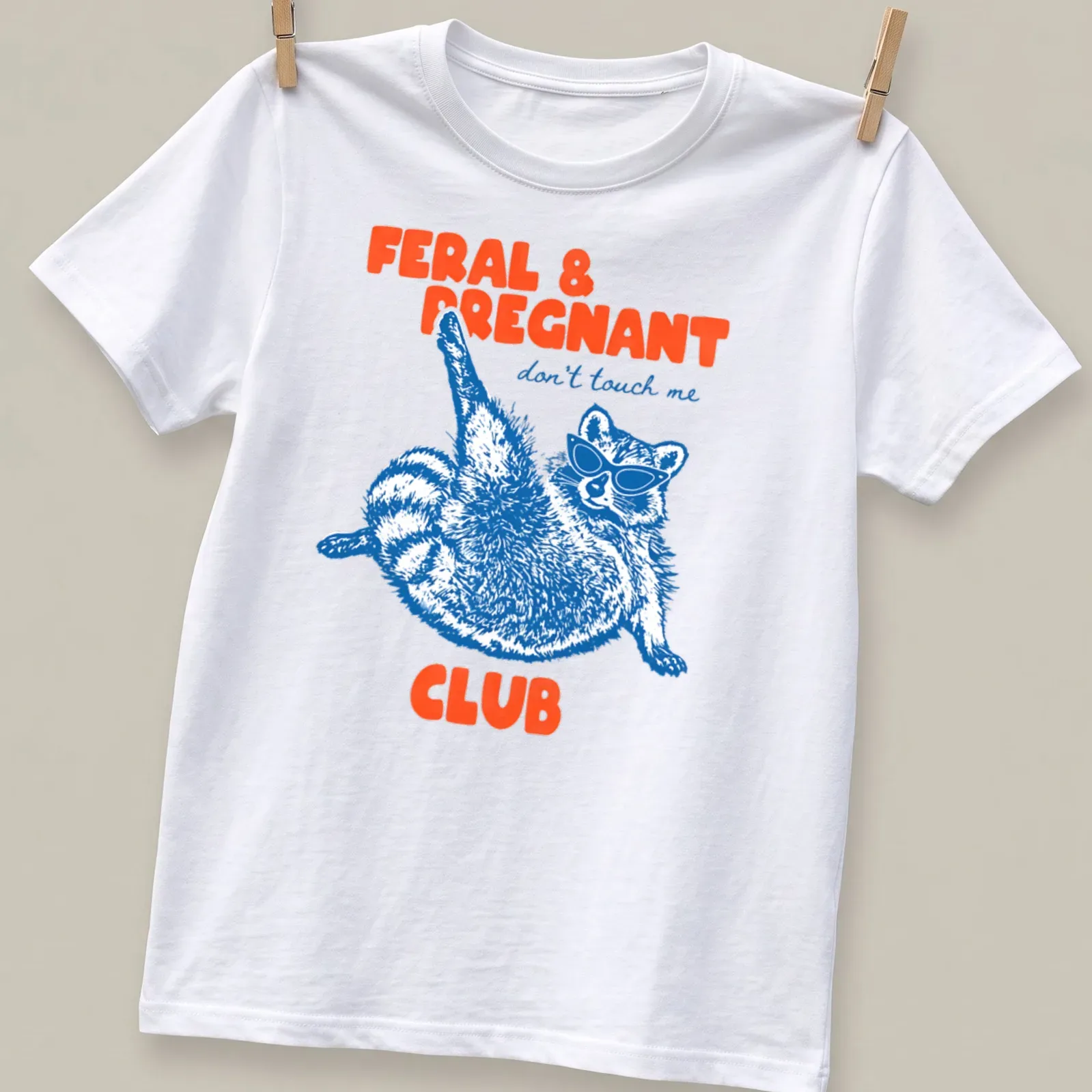 Playful illustration of a raccoon in sunglasses with text about being pregnant and feral — printed on a unisex t-shirt