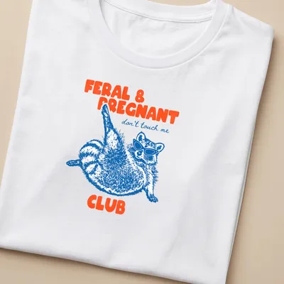 Playful illustration of a raccoon in sunglasses with text about being pregnant and feral — printed on a women's shirt