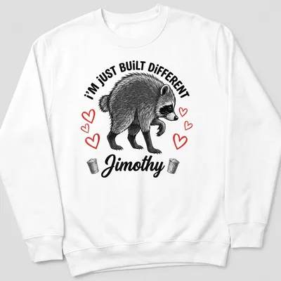 Illustrative t-shirt featuring raccoon and text 'I'm Just Built Different Jimothy' in black, white, and red. — printed on a unisex sweatshirt