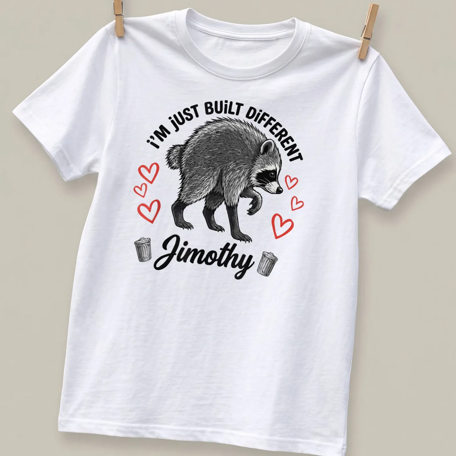 Illustrative t-shirt featuring raccoon and text 'I'm Just Built Different Jimothy' in black, white, and red. — printed on a unisex t-shirt