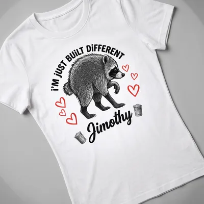 Illustrative t-shirt featuring raccoon and text 'I'm Just Built Different Jimothy' in black, white, and red. — printed on a women's shirt