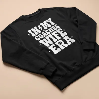 Bold typography t-shirt with IN MY COACHES WIFE ERA text in white — printed on a unisex sweatshirt