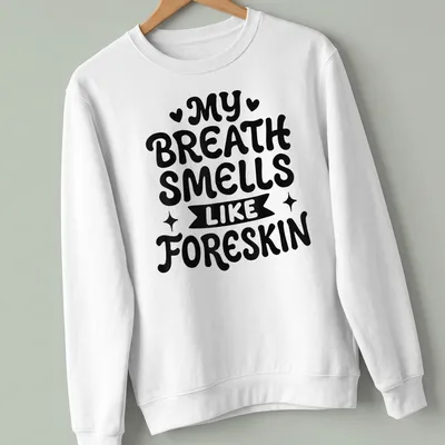 Bold humorous text saying My Breath Smells Like Foreskin in black and white — printed on a unisex sweatshirt