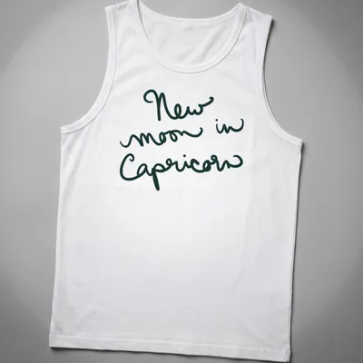 Handwritten script of 'New moon in Capricorn' in dark green text — printed on a tank top