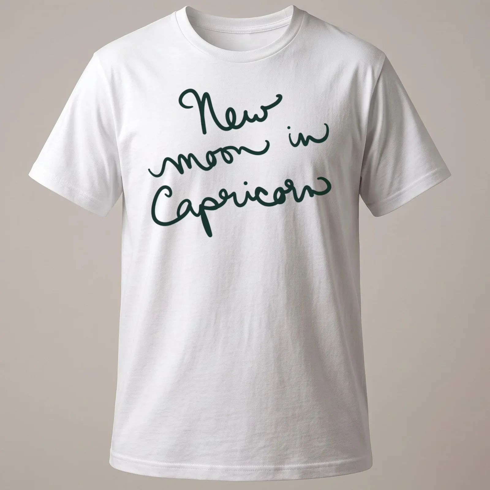 Handwritten script of 'New moon in Capricorn' in dark green text — printed on a unisex t-shirt