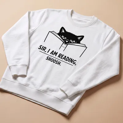 Bold line-art of a cat reading a book with text: 'SIR, I AM READING, SHOOSH.' — printed on a unisex sweatshirt